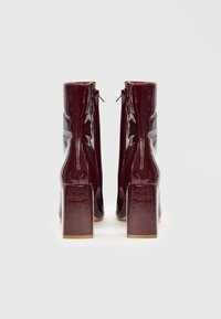 Botas de tobillo de charol burdeos con tacones cuadrados, con un acabado liso y brillante y una cremallera lateral para facilitar su uso.