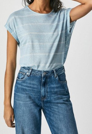 Person, die ein hellblaues kurzärmeliges gestreiftes T-Shirt trägt, das in hoch taillierte blaue Jeans mit Knopf und Gürtelschlaufen gesteckt ist.