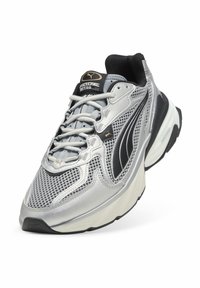 Sneaker argento e nero con tomaia in mesh, collo imbottito, lacci e suola bianca spessa con dettagli testurizzati. Logo del marchio visibile sulla linguetta.