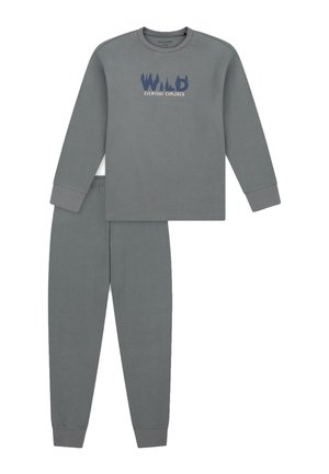 Smiling child balancing on one leg wearing gray long-sleeve top and pants with "WILD Everyday Explorer" text, barefoot on white background.