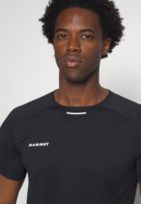 Schwarzes Performance-T-Shirt mit kurzen Ärmeln, featuring ein weißes Logo "MAMMUT" und einem horizontalen weißen Akzent auf der Vorderseite. Glatte Textur.