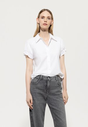 Weißes Hemd mit kurzem, gerafftem Ärmel, kombiniert mit hochgeschnittenen, hellgrauen Jeans. Glatter Stoff, klassisches Kragen-Design.