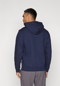Hoodie bleu marine en tissu doux, avec capuche à cordon de serrage, poignets côtelés et poches latérales. Design simple sans motifs visibles.