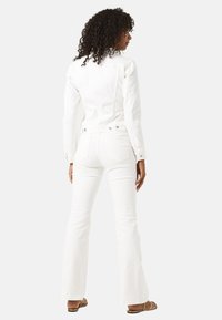 Chaqueta de mezclilla blanca con un diseño ajustado, mangas largas y botones de presión. Combinada con unos vaqueros acampanados blancos, que muestran una textura suave.