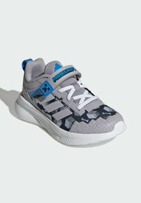 Gray athletic shoe with a textured fabric upper, blue accents, and a camo pattern. Features adjustable strap and cushioned sole.