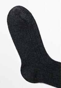 Zwarte wollen sok met geribbelde textuur en versterkte teen. Gladde afwerking met een lichte glans, taps toelopend naar de bovenrand.