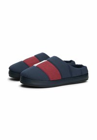 Pantofole slip-on blu navy con dettagli a righe rosse e bianche, tomaia in tessuto morbido, design imbottito e suola nera testurizzata.
