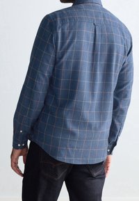 Camicia di flanella a scacchi blu con maniche lunghe, caratterizzata da linee a griglia verdi e rosa, polsini abbottonati e orlo curvo. Tessuto testurizzato.
