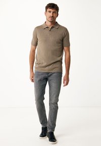 Kaki kortärmad polo med krage, tillsammans med slim-fit grå jeans och svarta snörskor mot en neutral bakgrund.