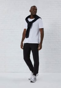 Camiseta branca, suéter preto amarrado aos ombros, calças pretas e ténis cinzentos. Tecido suave, corte descontraído e palete de cores neutras.
