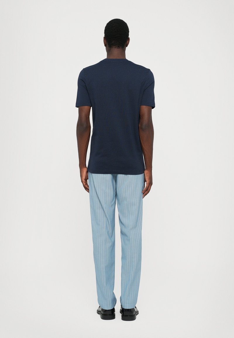 Camiseta de manga corta azul marino combinada con pantalones de rayas finas en azul claro, con un corte relajado y un sencillo cuello redondo, vista desde la parte de atrás.