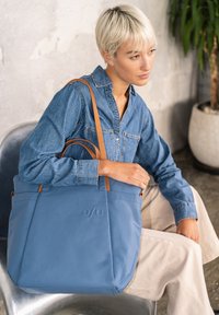 Borsa tote blu con manici in pelle marrone, realizzata in materiale leggero. Presenta un logo inciso sottile e un design elegante e strutturato.