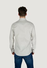 Camicia a maniche lunghe in tessuto grigio chiaro con un sottile motivo geometrico. Presenta un colletto classico e polsini con bottoni. Abbinata a jeans blu.