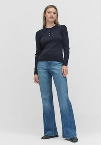 Marineblauwe geribbelde lange mouwen top met knoopkraag, gecombineerd met flared blauwe jeans. De outfit heeft een casual maar gestructureerde pasvorm.