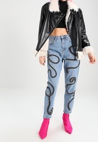 Svart konstläderjacka med vit syntetisk pälskrage, kombinerad med blå denimjeans med svart kedjeliknande broderi och klarr öda ankelstövlar.