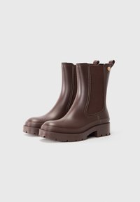 Bottes Chelsea en cuir marron avec des semelles épaisses et des panneaux élastiques sur le côté, photographiées sur un fond neutre.