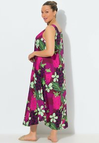 Ärmlös maxiklänning i lila med rosa blommor och gröna blad. Mjukt, flödande tyg med avslappnad passform. Bärs med platta sandaler.