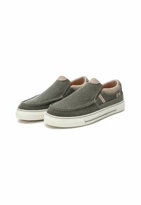Zapatos tipo slip-on en verde oliva con parte superior de tela texturizada, acentos beige en el talón y el cuello, y suela de goma blanca con diseño de múltiples capas.