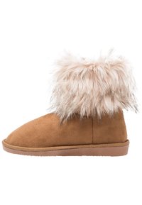 Botín de tobillo de ante marrón claro con un puño de piel de pelo suave y marrón claro. La puntera redondeada y la suela de goma brindan un aspecto suave y texturizado.