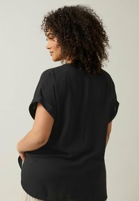 Blusa nera a maniche corte con vestibilità morbida, caratterizzata da una superficie testurizzata e un orlo curvo. La parte posteriore presenta un collo arrotondato e maniche arrotolate.