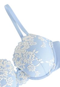 Valkoinen pitsireunuksinen vaaleansininen rintaliivi, jossa on pehmustetut kupit ja ohuet säädettävät olkaimet. Teräväkulmat ja sileä pinta.