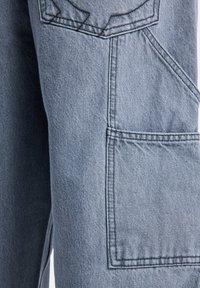 Light blue denim fabric with detailed stitching and a large rectangular patch pocket on a garment.