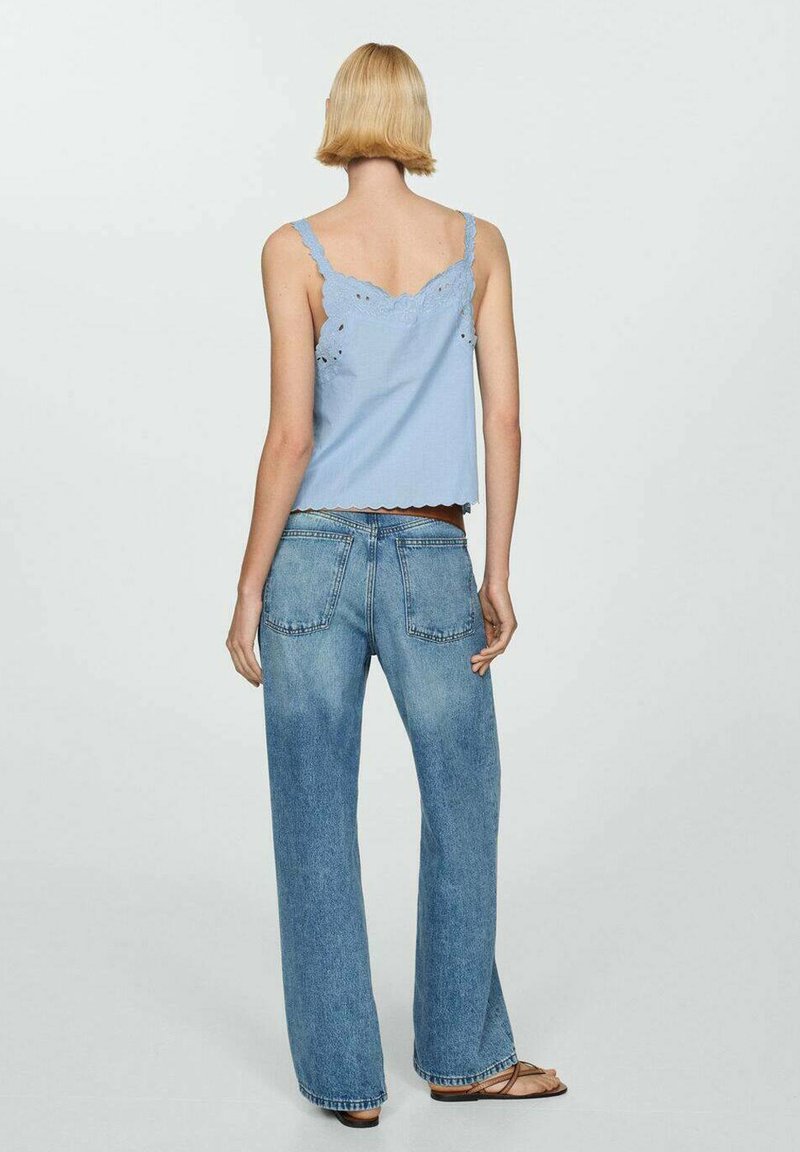 Jasnoniebieski top bez rękawów z falbaniastymi krawędziami, w połączeniu z luźnymi niebieskimi dżinsami. Widok z tyłu ukazuje delikatne szczegóły na topie.