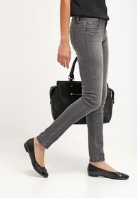Jeans grises con corte slim y un ligero estiramiento, combinados con bailarinas negras y un bolso negro, mostrando un diseño simple y moderno.
