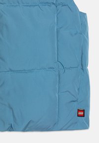 Απαλή μπλε πούφφερ τζάκετ με σχεδίαση σε καπιτονέ, διαθέτει ετικέτα με το λογότυπο LEGO. Λείος υφασμάτινος τύπος με ενισχυμένες ραφές και πλαϊνές τσέπες.