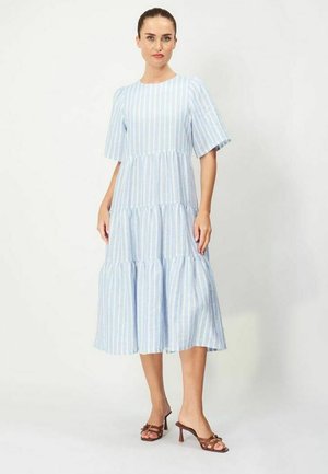 Kvinde iført en lyseblå og hvid midi-kjole med lodrette striber, korte ærmer og brune sandaletter med hæl.