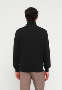 Μαύρο φούτερ με ψηλό γιακά, ρ ιμπ μανσέτες και τελείωμα; λεία υφή και απλό σχέδιο; φαίνεται από πίσω.