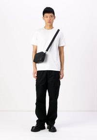 Černé cargo kalhoty, bílé tričko a malá černá crossbody taška. Oblečení má volný střih a masivní černé boty.