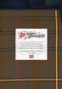 Rjav kariran material z rumenimi in rdečimi črtami; vsebuje belo oznako, ki podrobno opisuje blagovno znamko, material in obrtništvo od leta 1880.