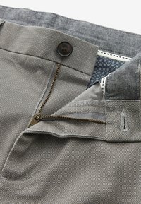 Tissu gris à motifs avec une braguette à zip et une fermeture à bouton, présentant une doublure intérieure contrastante avec un petit motif floral.