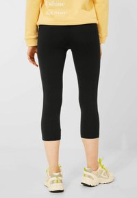 Black capri leggings with a smooth texture, featuring a fitted design. Paired with beige and neon green sneakers.