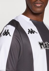 Sort-hvid stribet atletiktrøje med rund halsudskæring, med en logo foran og to sorte logoer på skuldrene.