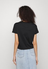 Černé zkrácené tričko s kulatým výstřihem a krátkými rukávy, kombinované se světle modrou džínovou sukní s dvěma zadními kapsami.