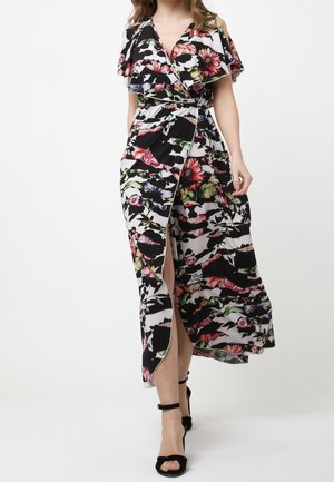 Mujer que lleva un vestido cruzado floral en blanco y negro con mangas con volante y una abertura alta en el muslo, combinado con tacones negros con correa en el tobillo.