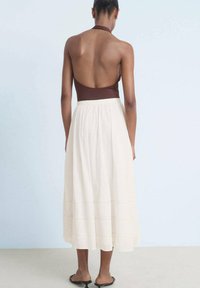 Brown halter top with open back, paired with a flowing cream maxi skirt featuring subtle stitching details. Textured fabric, relaxed fit.