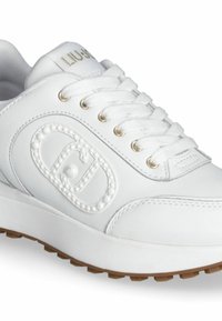 Bílá kožená teniska s kulatou špičkou, polstrovaným jazykem a šněrováním vpředu. Obsahuje ražené logo a zlaté kovové očka. Pryžová podrážka.