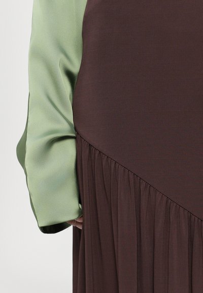 Brun kjole med en samlet nederdel, der har en kontrasterende lys grøn satinsleeve, glat tekstur og diagonale sømdetaljer.
