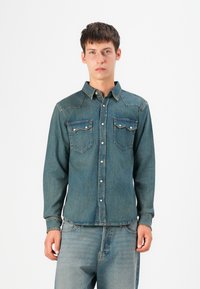 Denim Hemd mit Knöpfen in Mittelblau, ausgestattet mit zwei Brusttaschen, einer spitzen Passe und silberfarbenen Druckknöpfen. Lange Ärmel mit knopfbaren Manschetten.