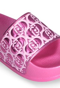 Pink slide sandal with a textured strap featuring a cut-out logo pattern. The sole is solid pink, and the material appears synthetic and glossy.