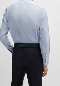 Modrá a bílá pruhovaná košile s dlouhými rukávy, střihem na tělo a manžetami na knoflíky, doplněná tmavými kalhotami a černým páskem.