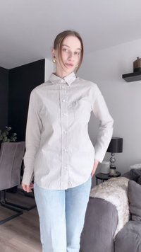 Camisa de botão às riscas em bege claro e branco, com colarinho, mangas longas e um ajuste relaxado. Combinada com jeans em azul claro.