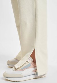 Cremefarvede sweatpants med side slids og en blød tekstur, parret med pastelfarvede sneakers med mesh- og ruskindsdetaljer.