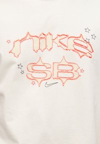 Κόκκινο κειμενογραφημένο «Nike SB» με μαύρα αστέρια και μικρό μαύρο λογότυπο Nike σε λευκό ύφασμα.