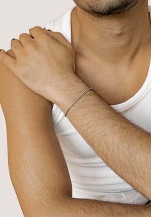 Silver metal bracelet on a wrist, featuring a smooth, round shape. The wrist is bare and the arm shows light hair, against a light background.