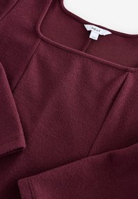 Bordowy sweter o fakturowanej tkaninie, kwadratowym dekolcie i długich rękawach. Posiada metkę z logo na dekolcie oraz staranne detale szycia.