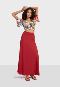Květinový crop top s širokými rukávy, spárovaný s dlouhou červenou sukní. Sukně má hladkou strukturu a pohodlný pas.